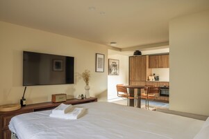 Una habitación de hotel con cama, escritorio, silla, televisión y kitchenette.