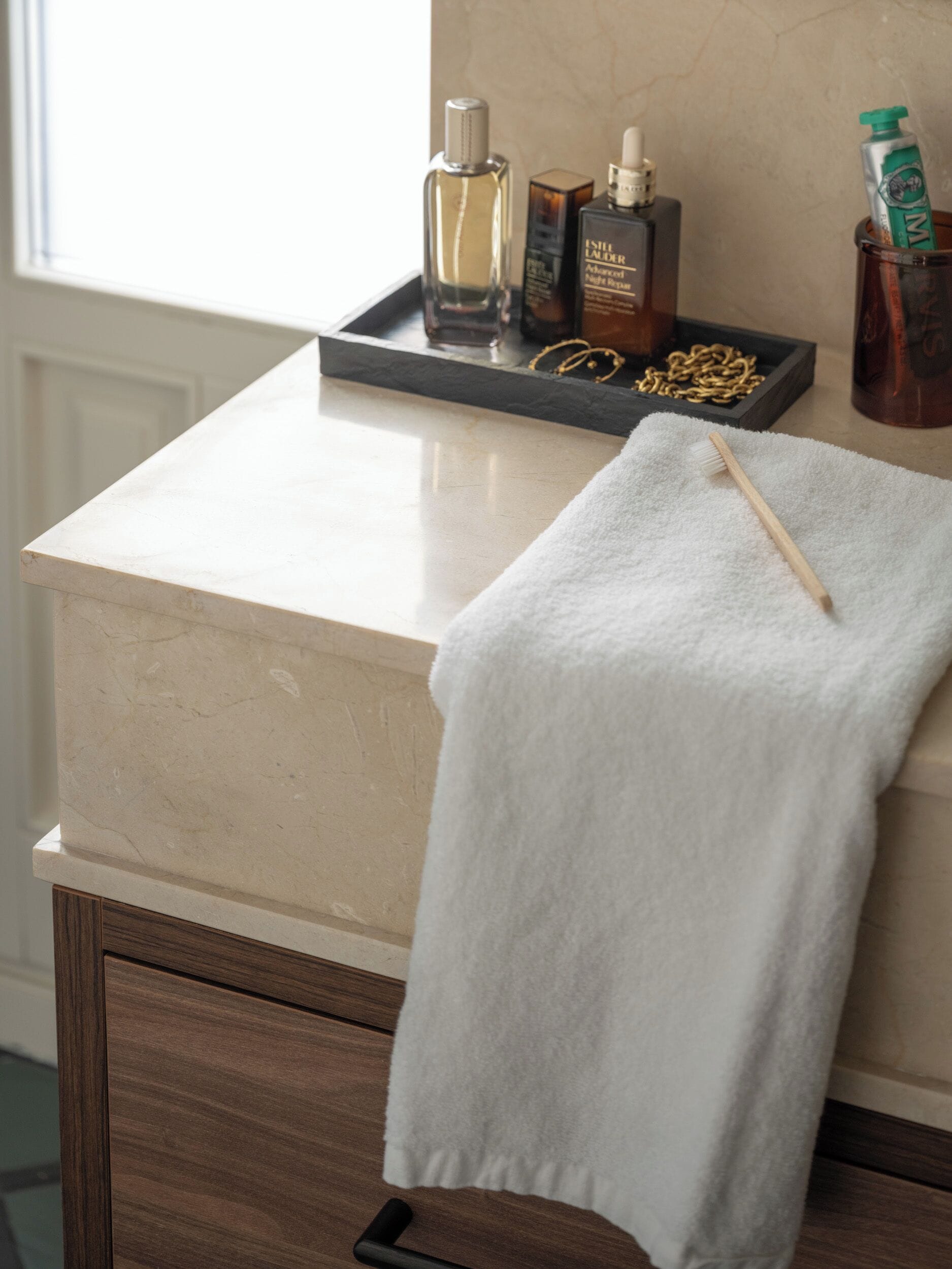 A bathroom with a white towel hanging on a wooden cabinet, a tray with toiletries, and a bottle of hand soap.