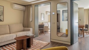 A modern hotel room with a sofa, a small table, a mirror, and a dining area with chairs. - POSTCODE Chueca (Madrid)