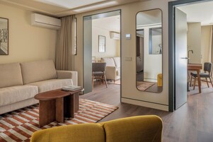 Una habitación de hotel moderna con sofá, una mesita, un espejo y un comedor con sillas.