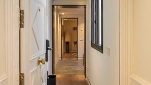 A hallway with a door on the left, a window on the right, and a trash bin in the center. - POSTCODE Chueca (Madrid)