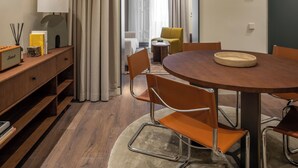 A modern hotel room with a wooden dining table, chairs, a lamp, a radio, and a view into the adjacent living area. - POSTCODE Chueca (Madrid)
