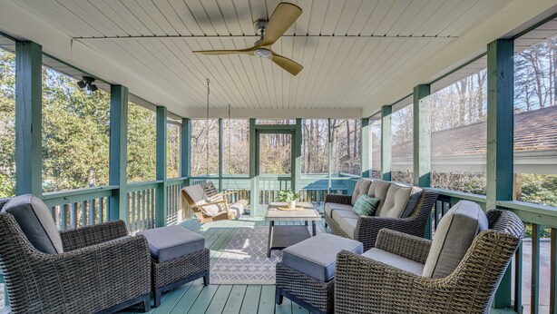 Eine überdachte Veranda mit Korbmöbeln, einem Deckenventilator und Blick auf Bäume sowie ein Haus im Hintergrund.