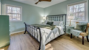 Ein Schlafzimmer mit Bett, Stuhl, Nachttisch, Lampe und Deckenventilator.