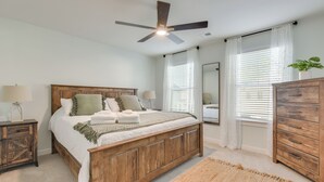 Une chambre à coucher avec un lit en bois, un ventilateur de plafond, une table de chevet, une commode et une grande fenêtre avec des stores.
