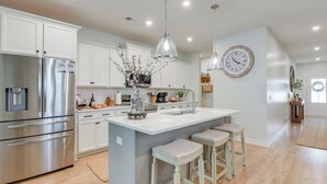 Une cuisine moderne avec des meubles blancs, des appareils en acier inoxydable et un îlot central doté de tabourets de bar.
