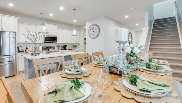 Une cuisine moderne avec des armoires blanches, des appareils en acier inoxydable et un coin repas aménagé pour un repas, avec une table en bois, des serviettes vertes et un centre de table décoratif.