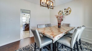 A dining room with a table set for six, surrounded by six chairs, a chandelier, and a decorative wall piece. - Walk to Lake! Home w/ Pool Near At&t Stadium (Rowlett)