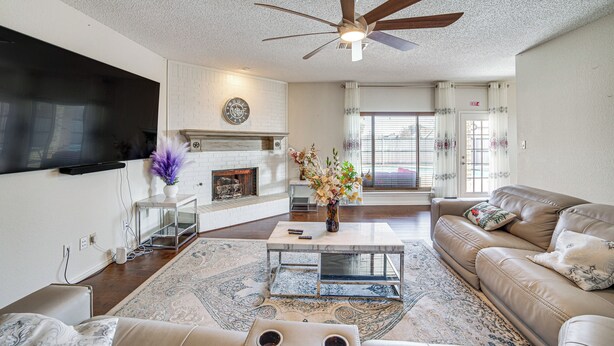 A living room with a fireplace, a ceiling fan, a flat-screen TV mounted on the wall, and a sofa. - Walk to Lake! Home w/ Pool Near At&t Stadium (Rowlett)