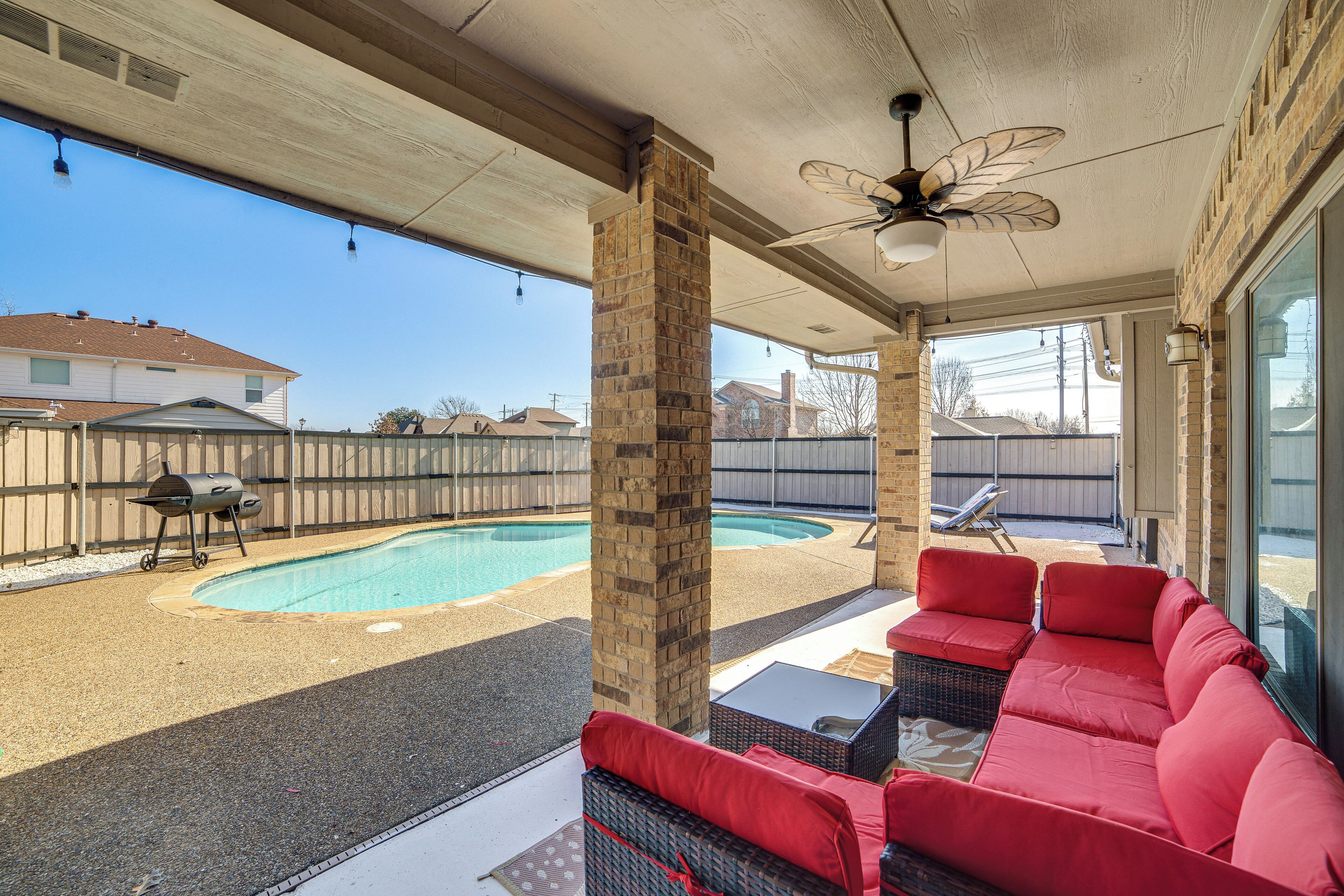 A covered patio with a pool, red outdoor furniture, and a ceiling fan.