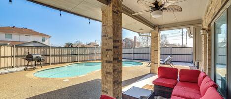 A covered patio with a pool, red outdoor furniture, and a ceiling fan.