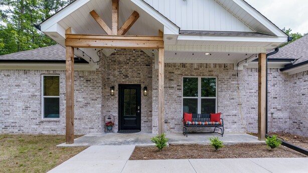 A brick house with a covered porch, a black front door, and a bench with red cushions. - Steps to Fairway: Hot Springs Village Golf Retreat (Hot Springs Village)