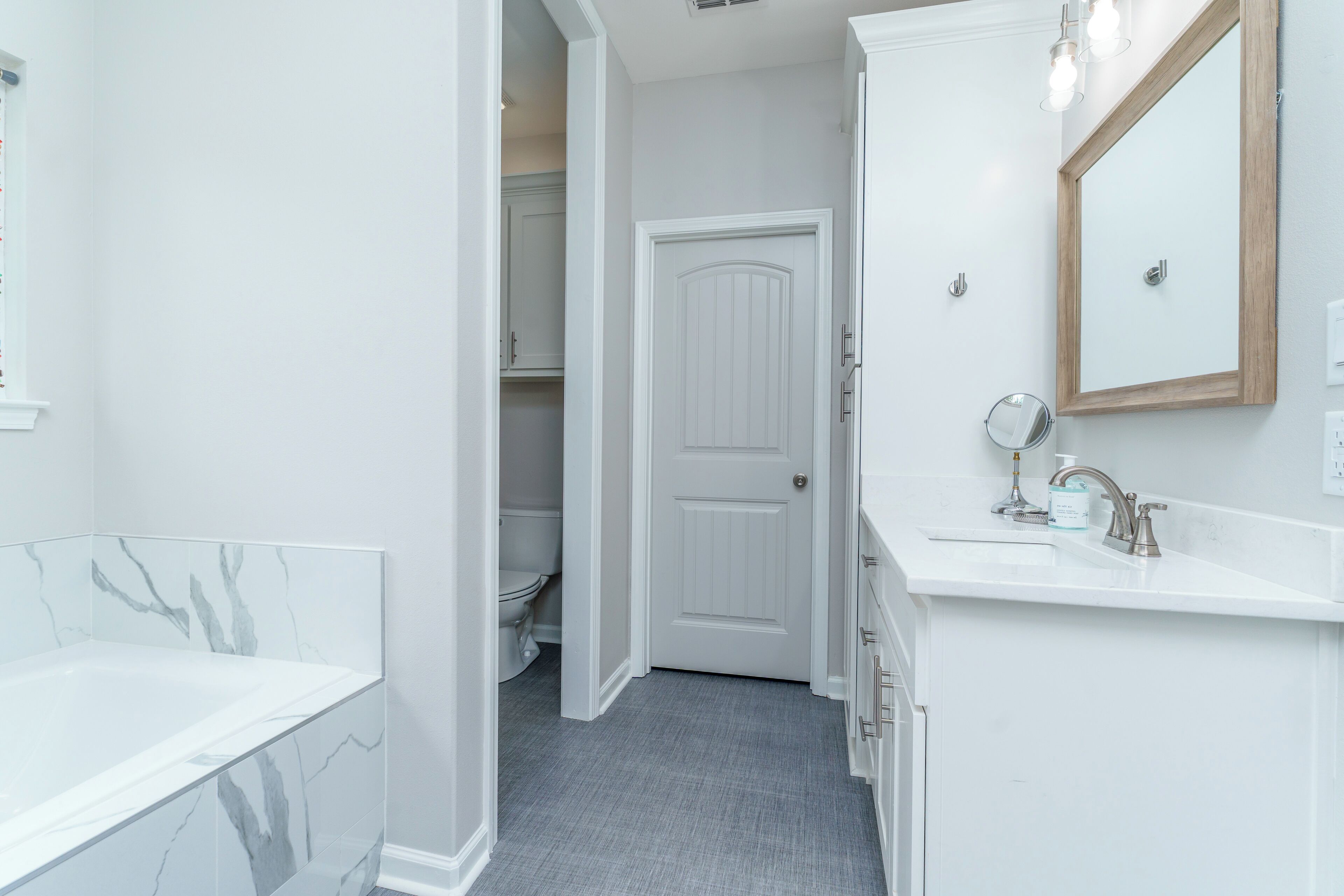 A bathroom with a marble bathtub, a white sink with a mirror, and a door leading to a toilet.