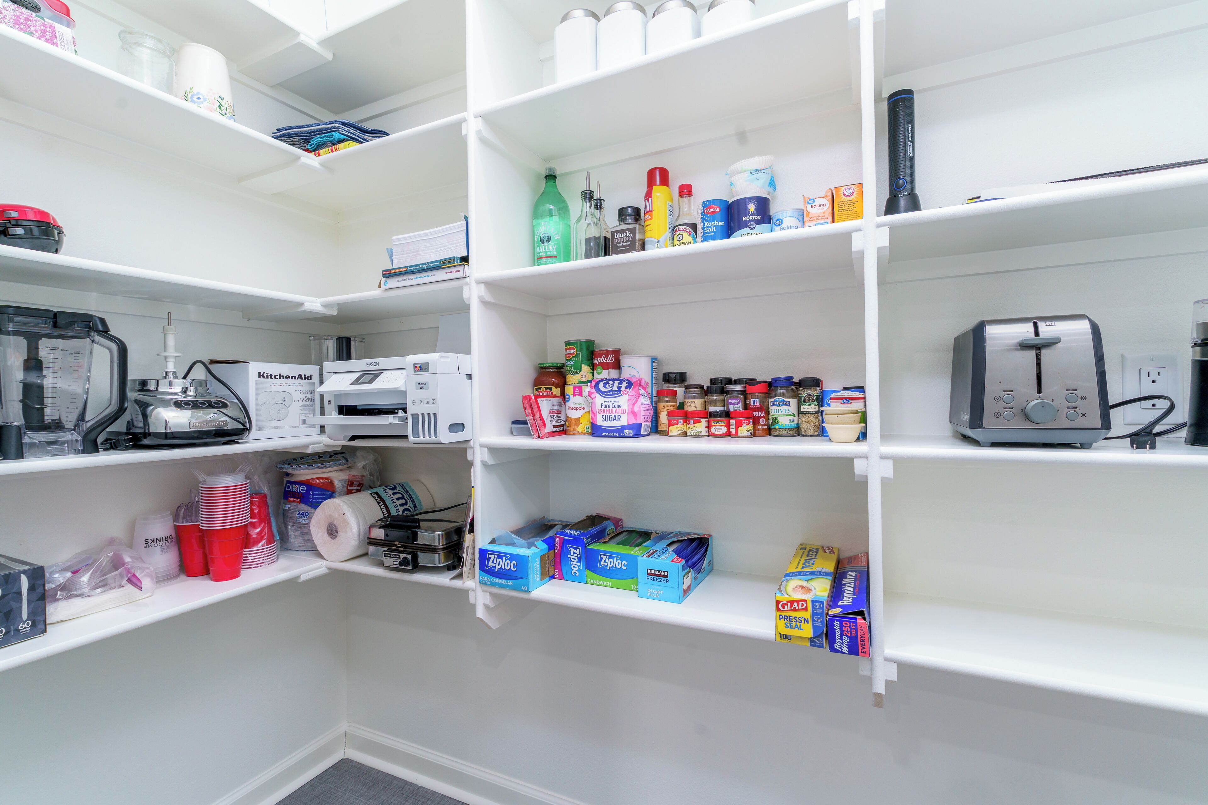 A well-organized pantry with shelves stocked with various food items, kitchen appliances, and storage containers.