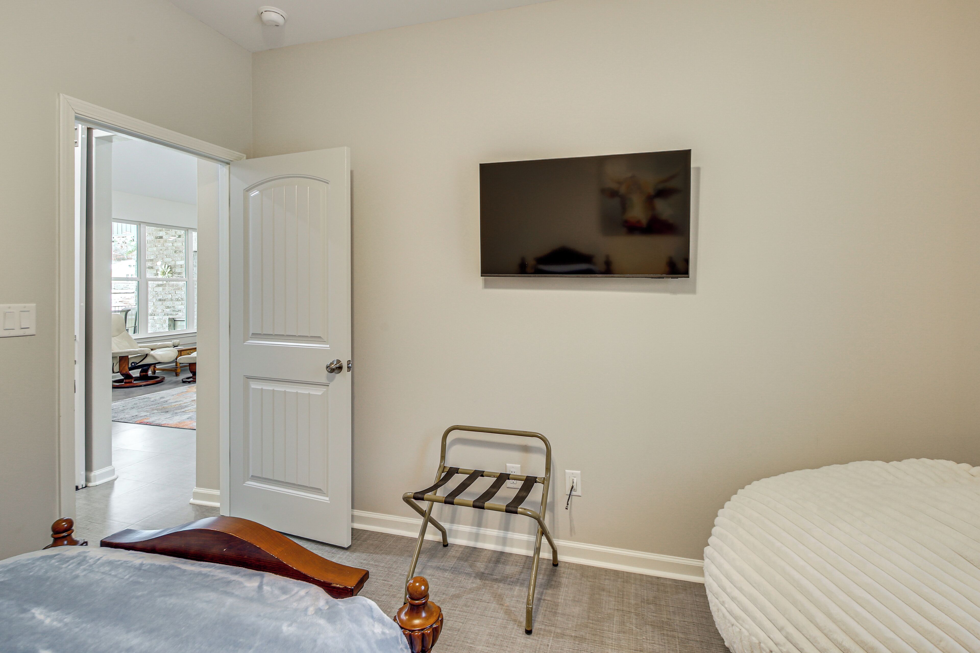 A bedroom with a bed, a chair, a door, and a wall-mounted TV.