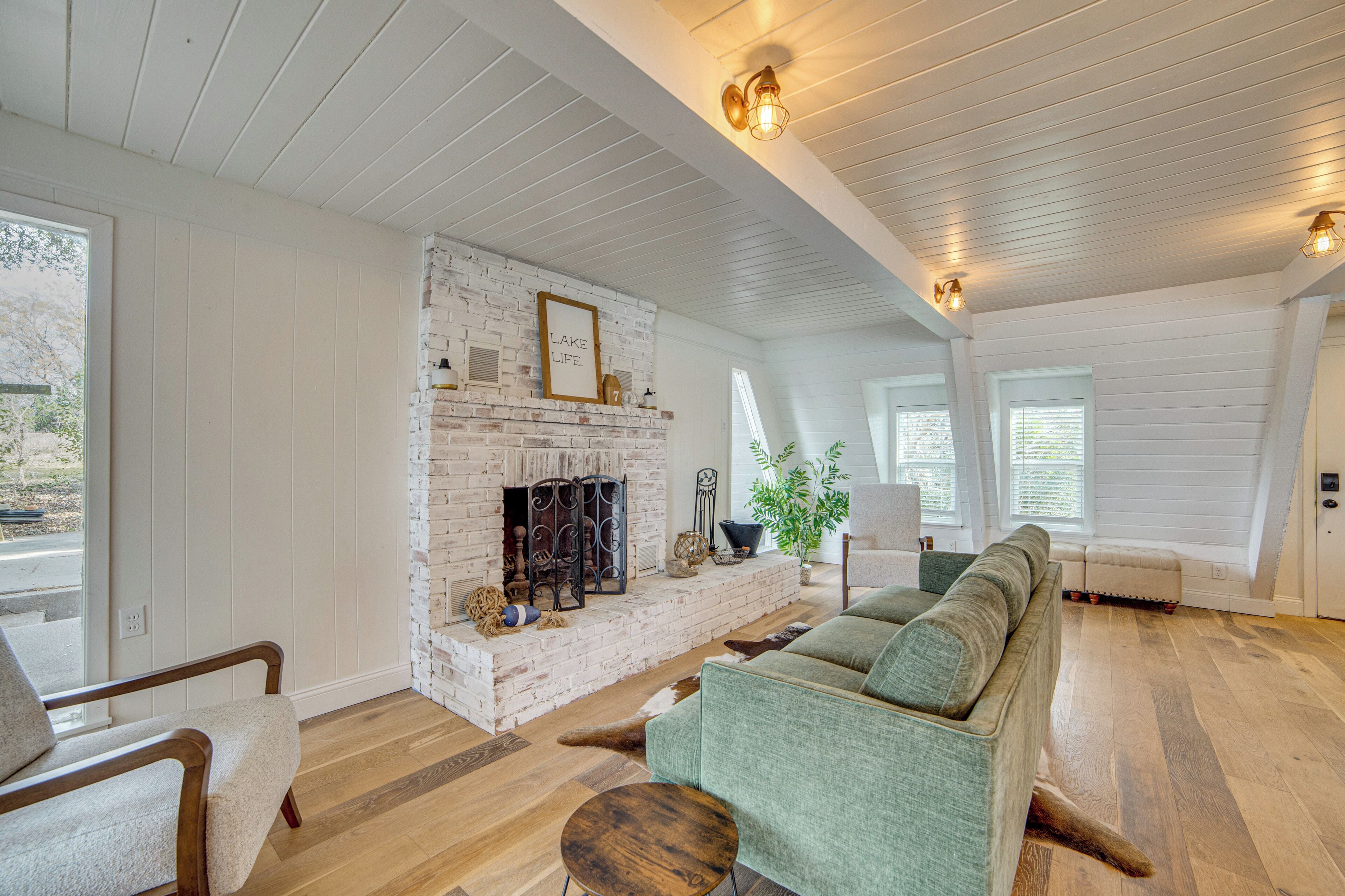 A cozy living room with a brick fireplace, wooden floors, and a green sofa.