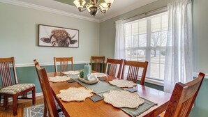 Une salle à manger avec une table en bois, des chaises, des sets de table et un lustre.