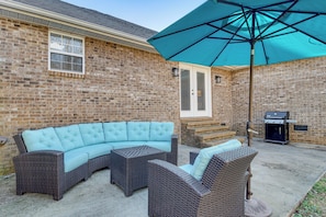 Une terrasse en briques avec un canapé modulable et deux fauteuils, un barbecue et un grand parasol.