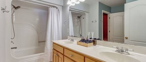A bathroom with a bathtub, two sinks, a vanity with drawers, a mirror, and a shower.