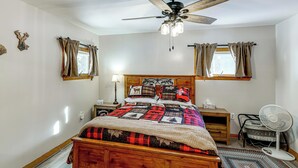 A bedroom with a wooden bed, a ceiling fan, a nightstand, a lamp, a window with curtains, and a standing fan. - Waterfront Family Home w/ Seasonal Dock in Lincoln (Lincoln)