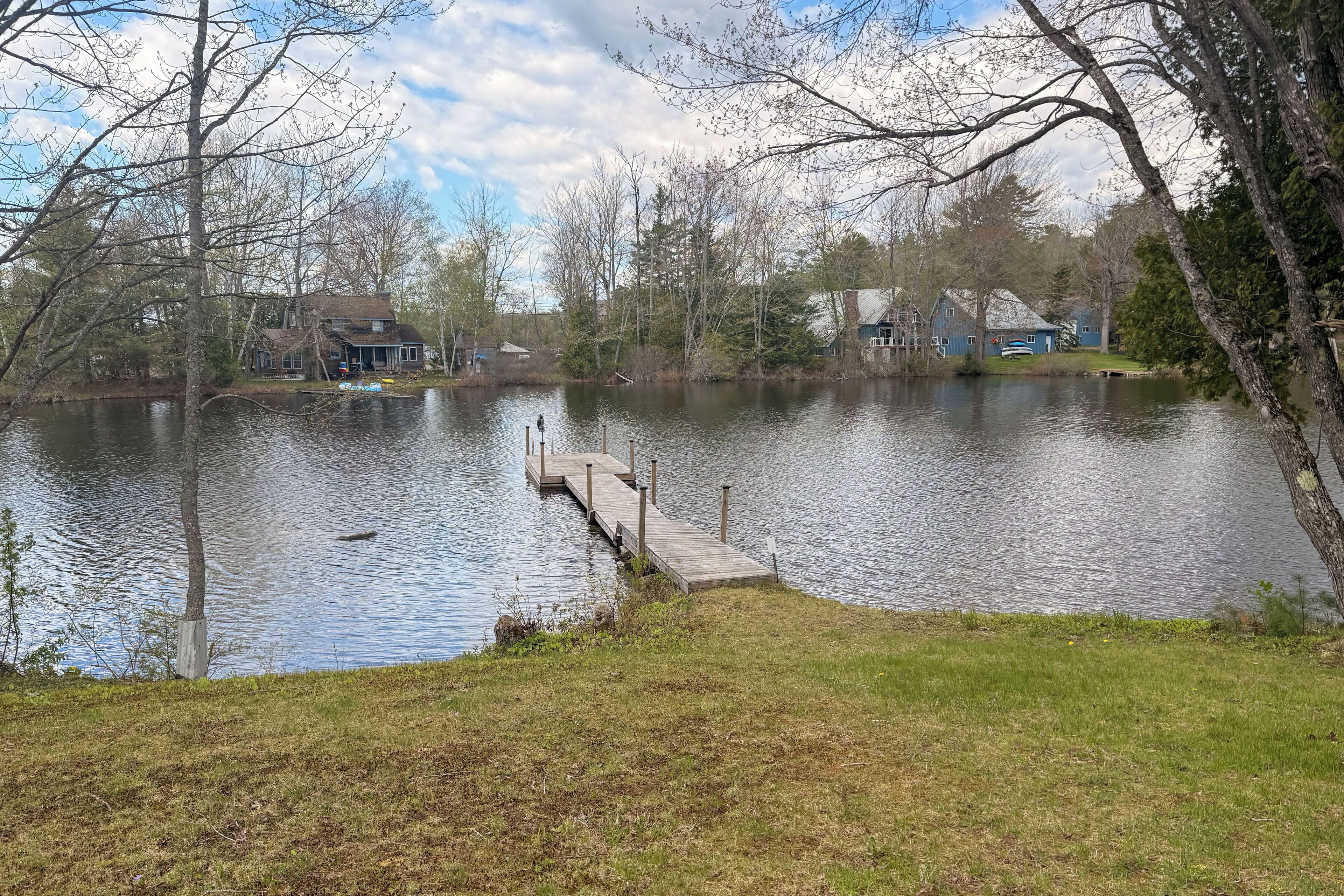 Un lac avec une jetée qui s’avance sur l’eau, entouré d’arbres et de maisons.
