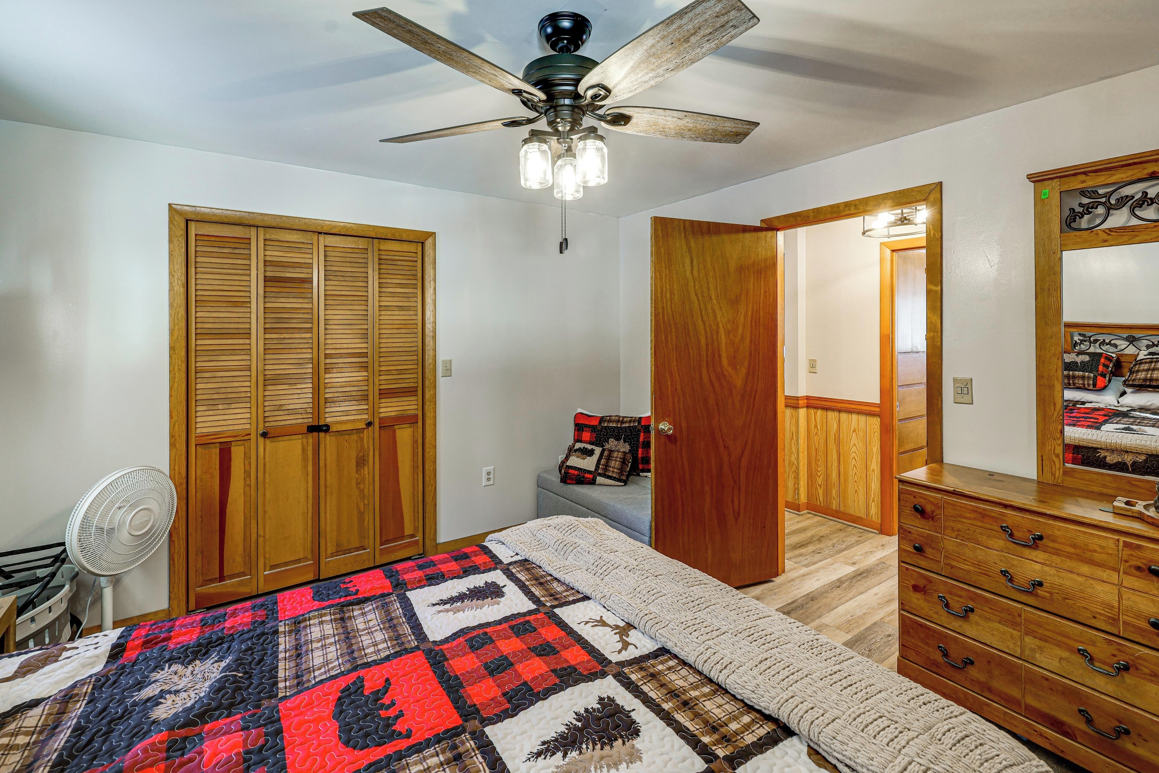 A bedroom with a bed, wooden wardrobe, dresser, ceiling fan, and a quilt.