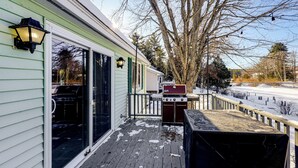 A covered deck with a grill and a barbecue, a sliding glass door, and a light fixture on a house with a green exterior. - Waterfront Family Home w/ Seasonal Dock in Lincoln (Lincoln)