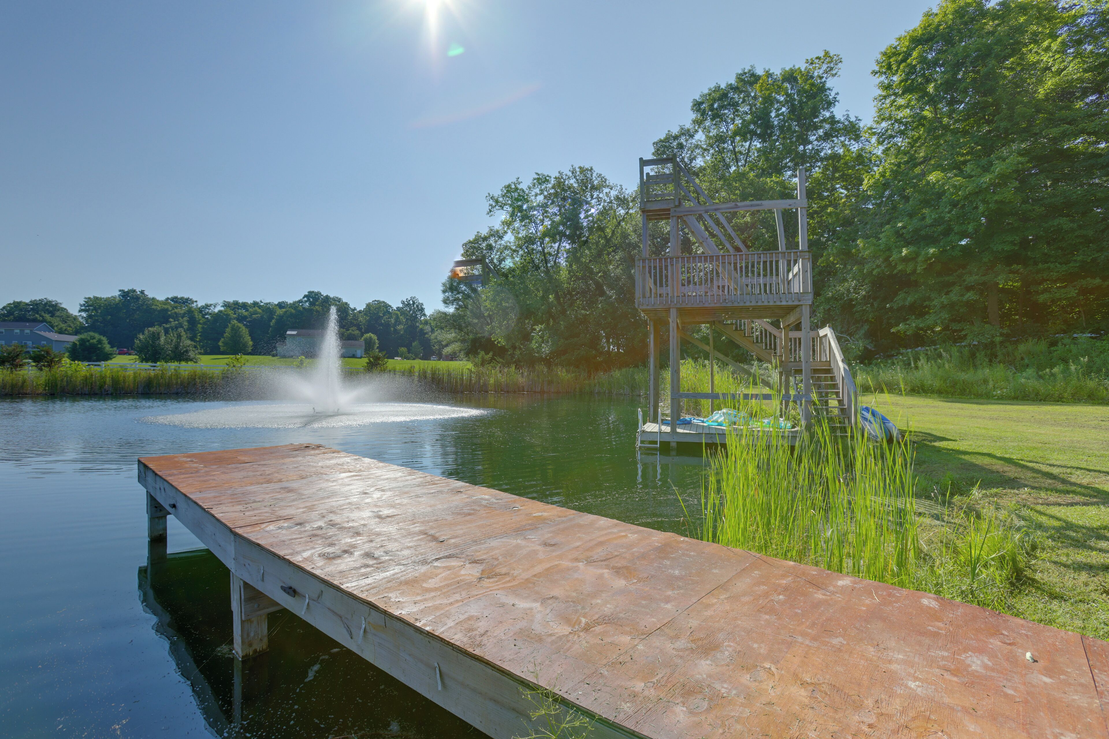 A wooden dock extending into a body of water with a fountain in the background.