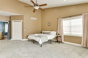 Une chambre à coucher avec un lit, un ventilateur de plafond, une fenêtre avec des rideaux et une porte.