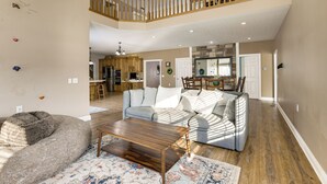 A spacious living room with a high ceiling, a wooden staircase, and a kitchen in the background. - Family Home on 9 Acres! Climbing Wall & Gym (Thornville)