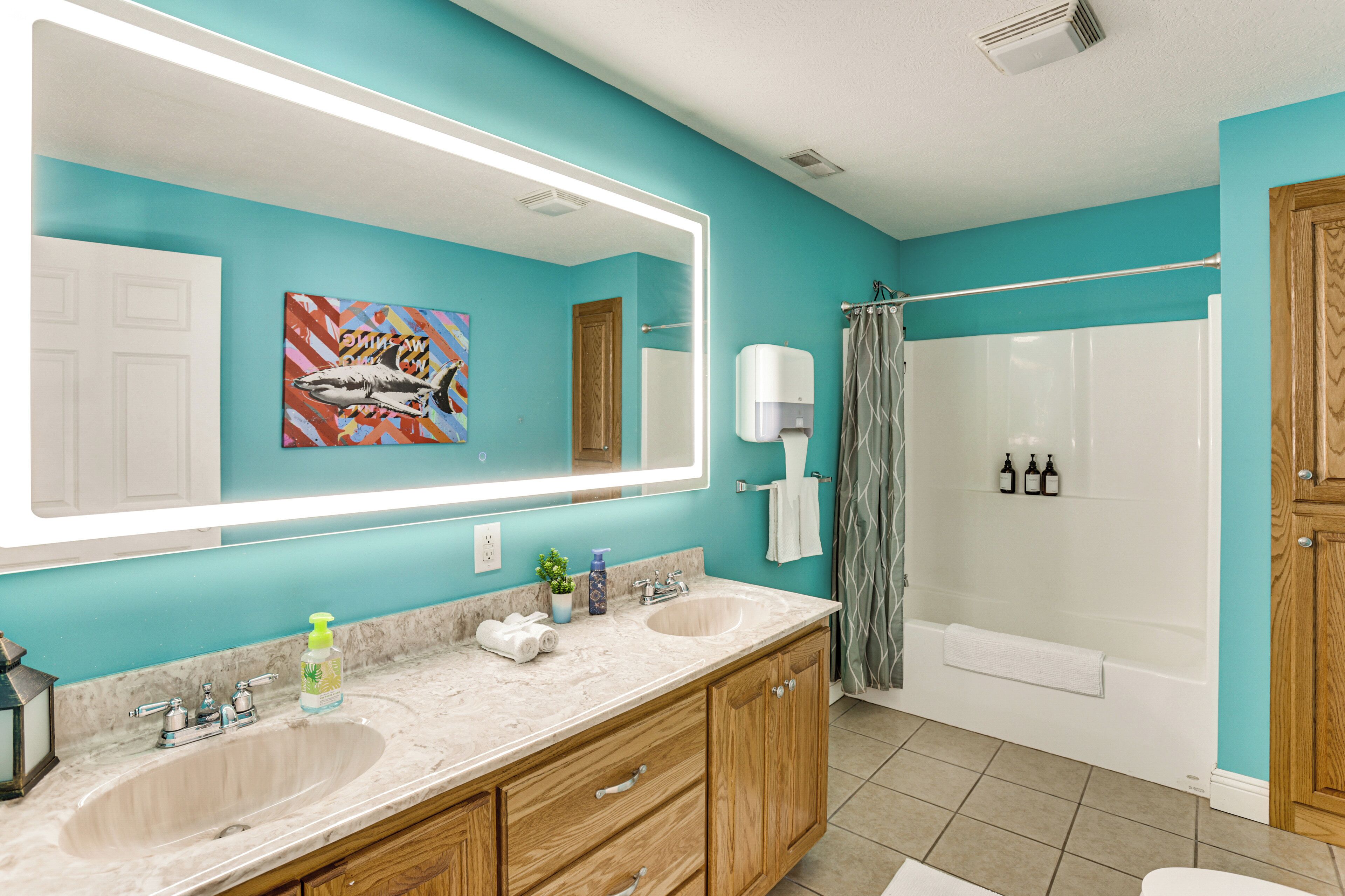 A bathroom with a large mirror, two sinks, a shower, and a towel rack.
