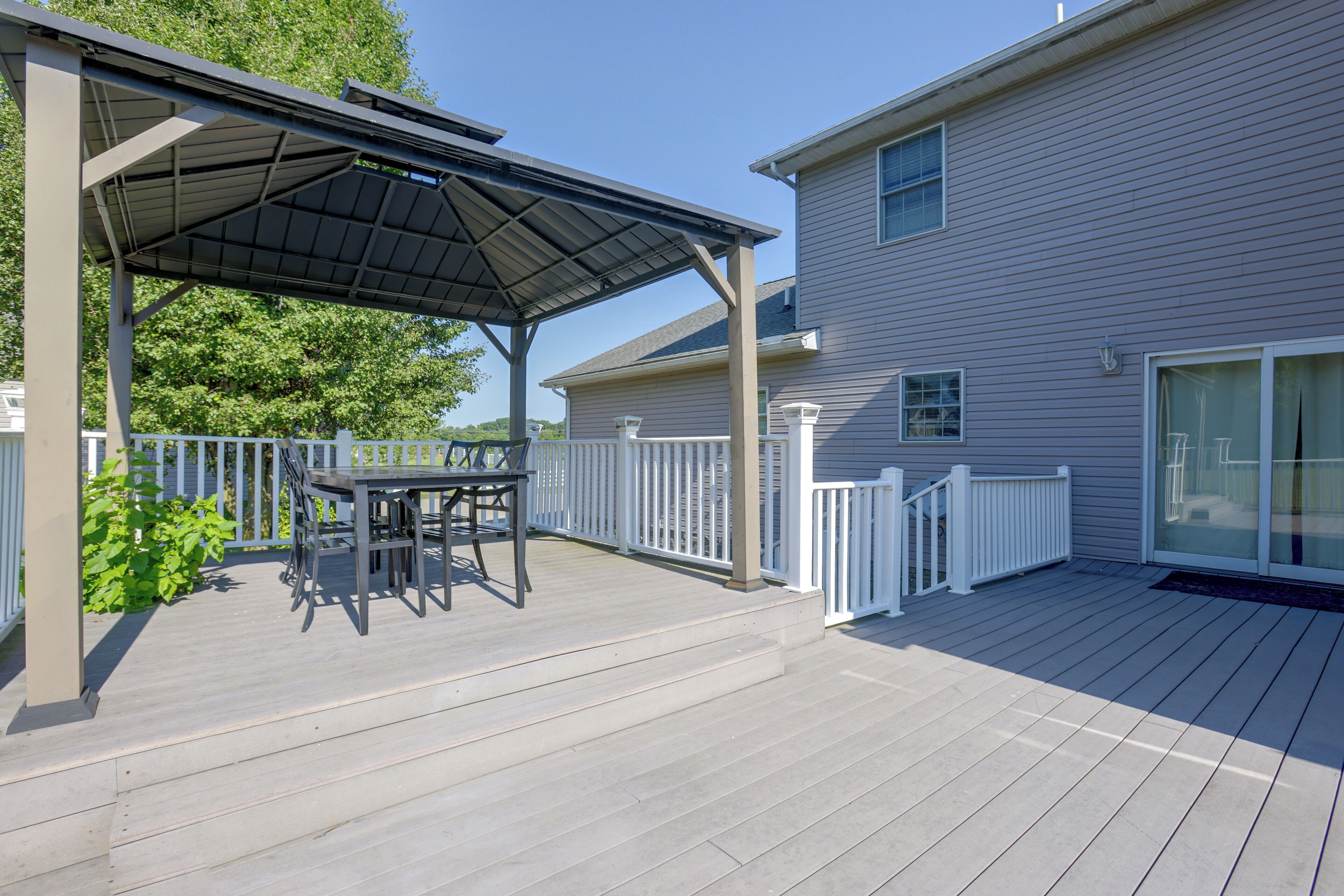 A covered patio with a table and chairs, a white fence, and a house with a garage door.