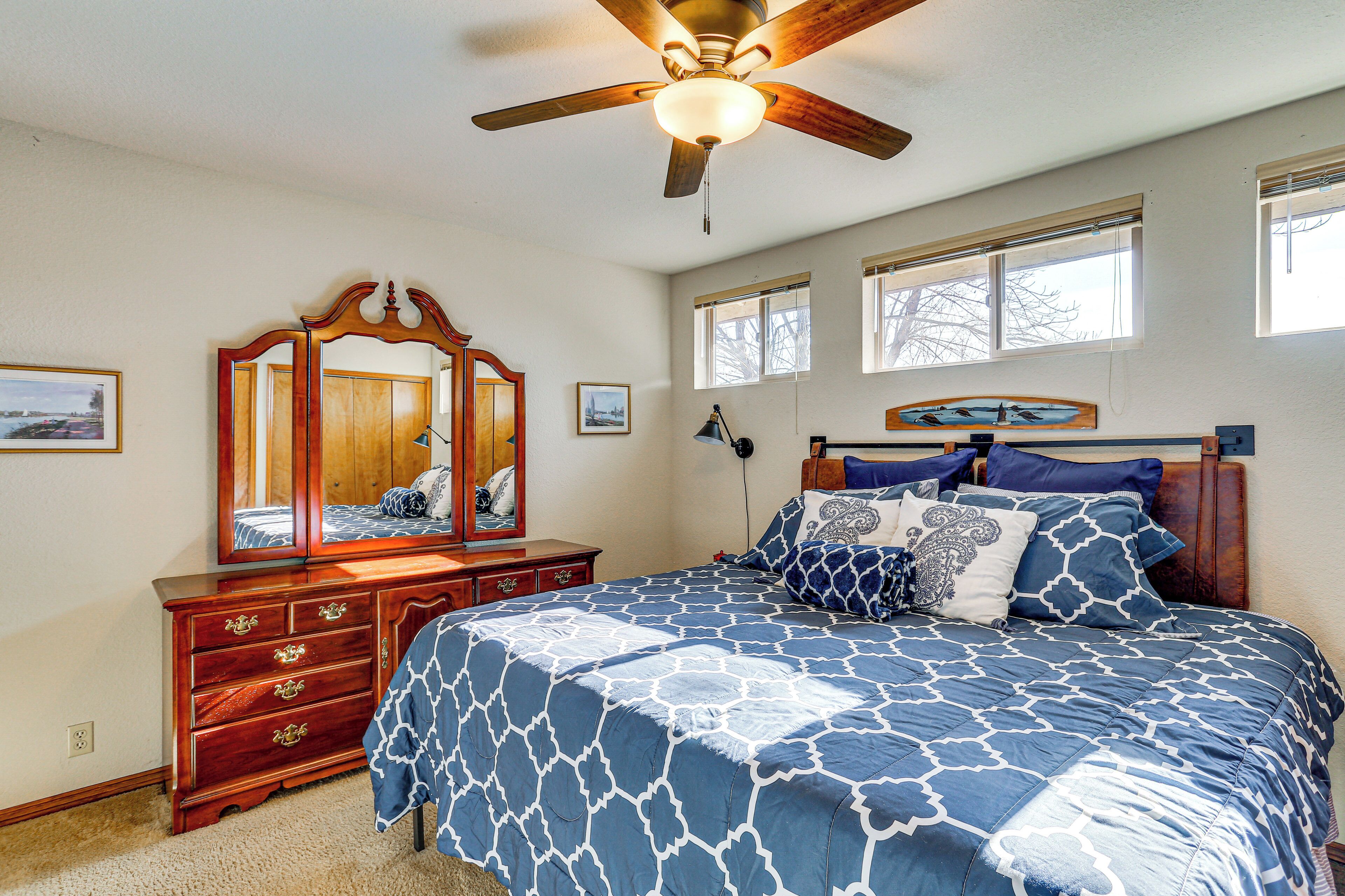 A bedroom with a bed, dresser, mirror, ceiling fan, and windows.