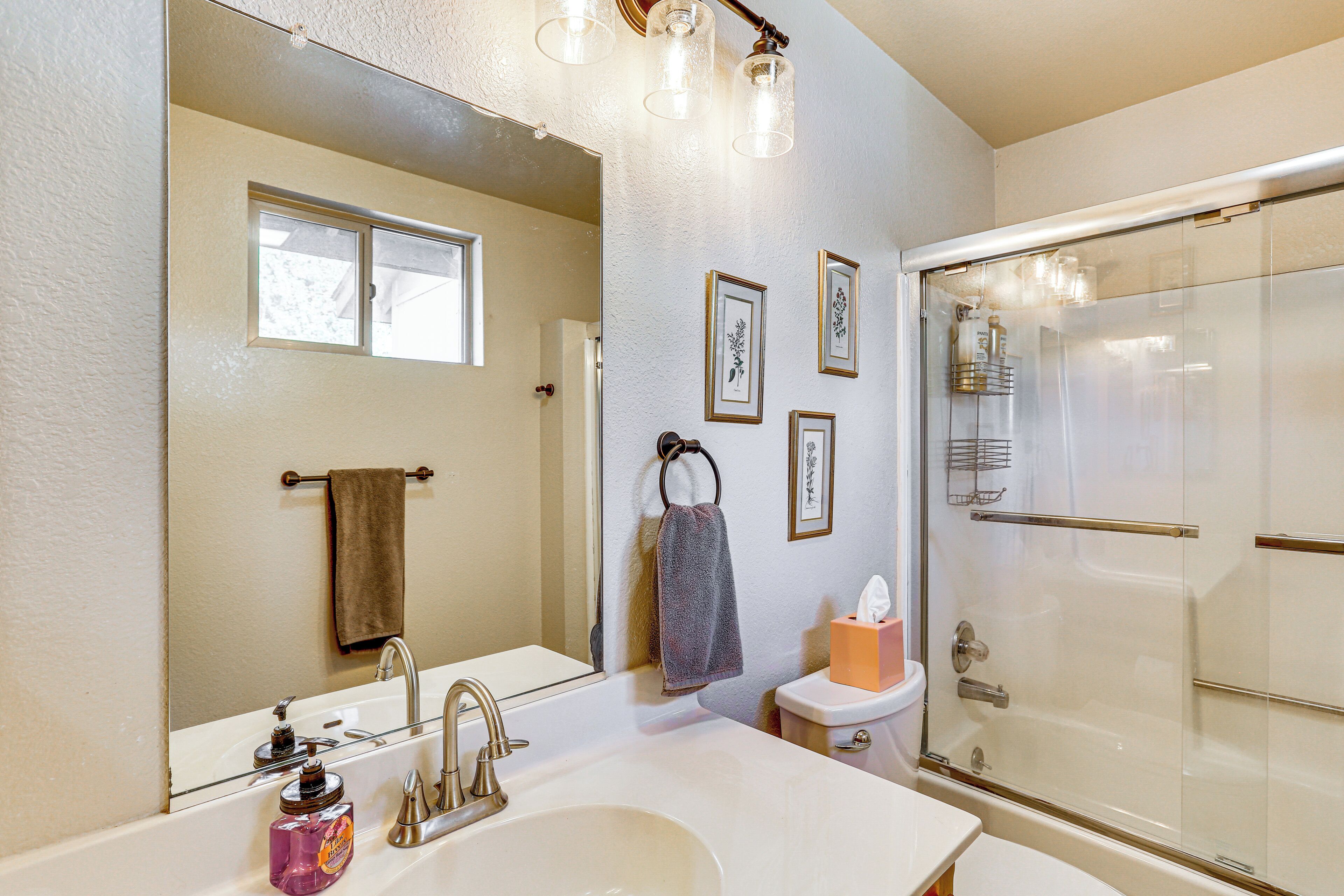 A bathroom with a large mirror, a sink, a toilet, and a glass-enclosed shower.
