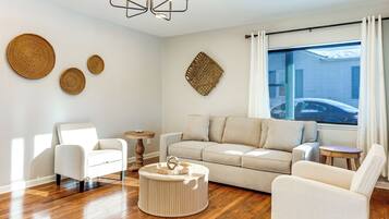 A modern living room with a beige sofa, two white armchairs, a round coffee table, and a chandelier.