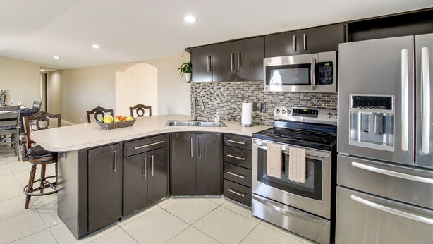 A modern kitchen with dark cabinets, stainless steel appliances, a microwave, oven, and a large island with a fruit bowl. - Stargaze & Unwind: Quiet Turpin Gem w/ Fenced Yard (Turpin)