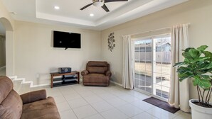 A spacious living room with a ceiling fan, a flat-screen TV mounted on the wall, a brown leather sofa, a recliner, and a potted plant. - Stargaze & Unwind: Quiet Turpin Gem w/ Fenced Yard (Turpin)