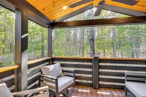 A covered outdoor seating area with wooden benches and a view of a forest.