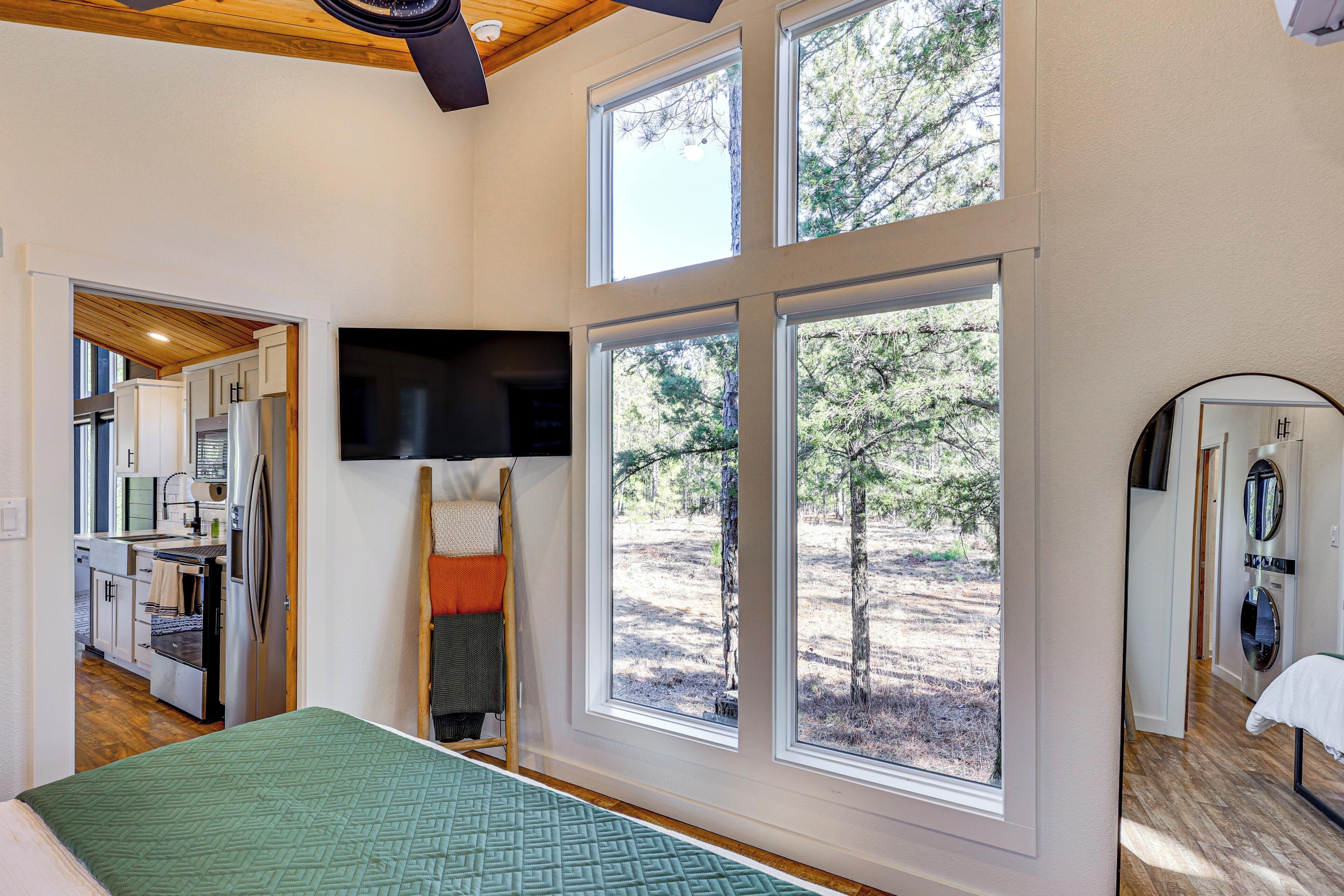 A bedroom with large windows, a bed, a TV, and a view of the outdoors.