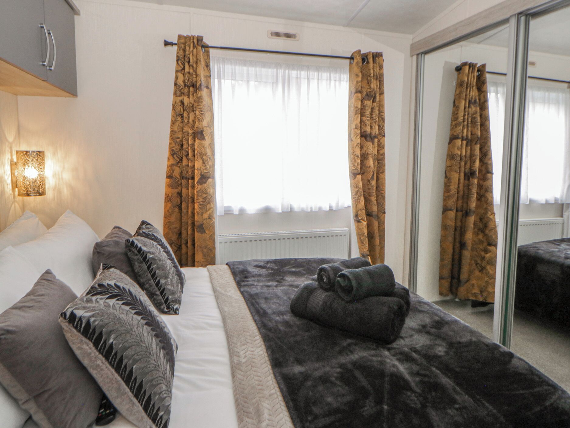 Habitación de hotel con cama, almohadas, una colcha, espejo y cortinas.