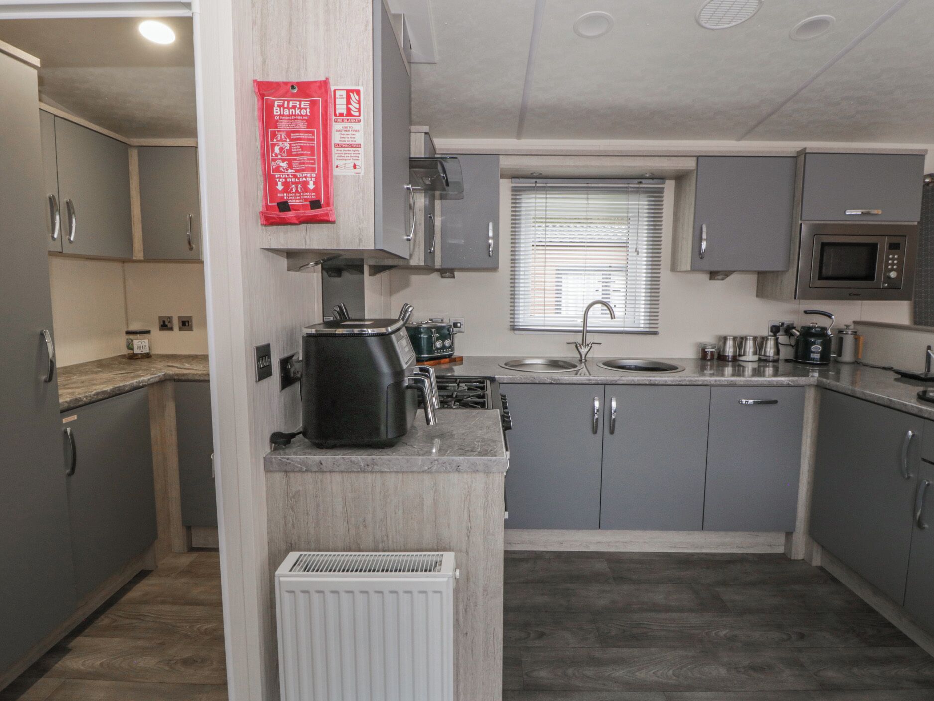 A compact kitchen with grey cabinets, a built-in microwave, a stove, and a red fire blanket hanging on the wall.