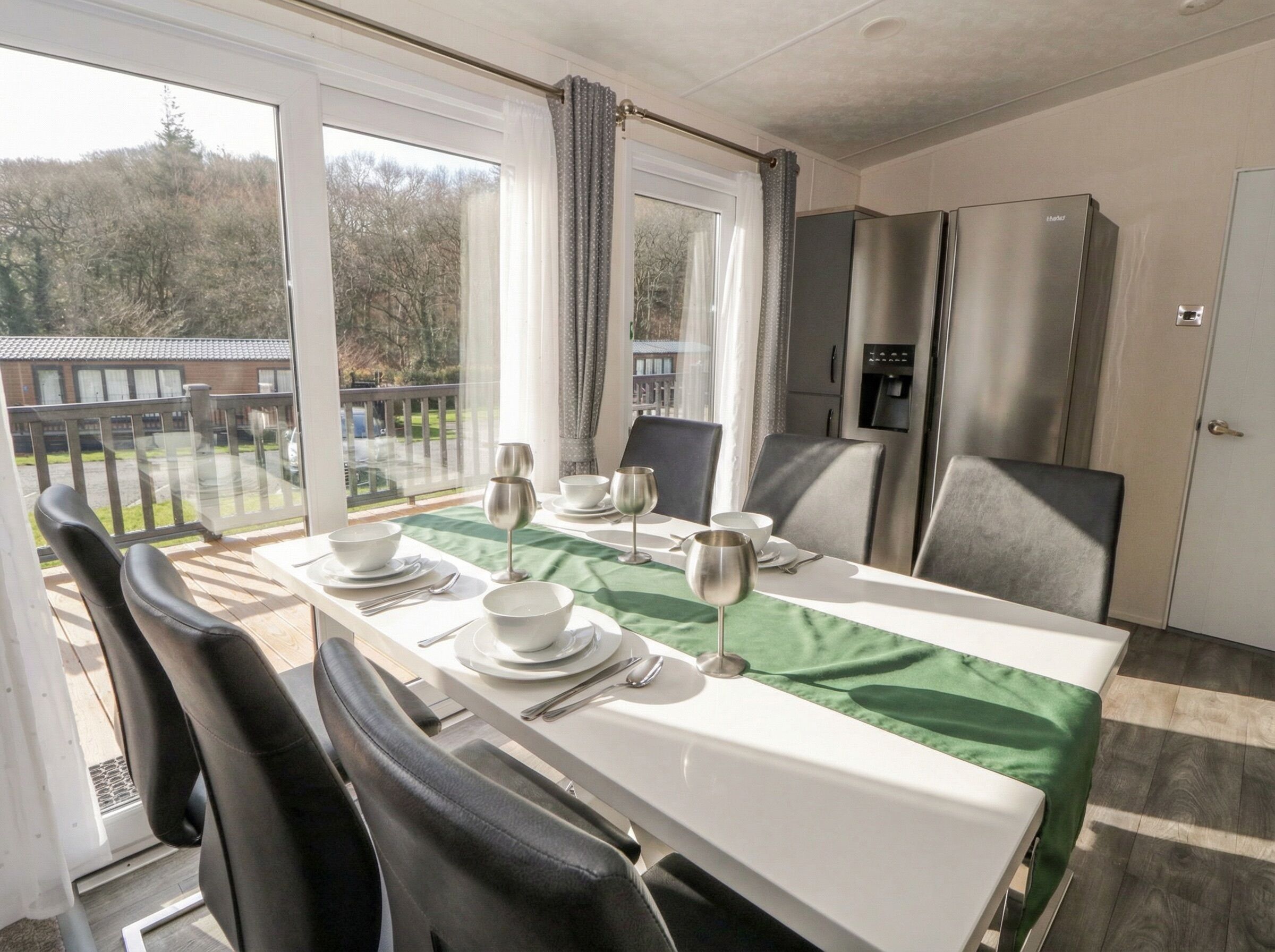 A dining area with a table set for four, chairs, a refrigerator, and a view of the outdoors.
