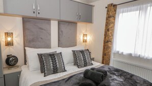 A modern bedroom with a large bed, grey cabinets, and a window with sheer curtains. - The Ridgeway (New Quay)