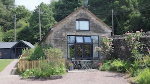 A stone cottage with a large window, a small garden, and a gravel path. - Horse Gin (Lydney)