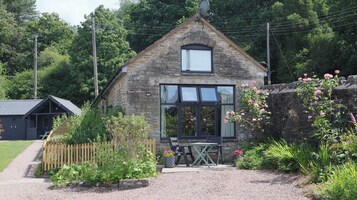 A stone cottage with a large window, a small garden, and a gravel path.