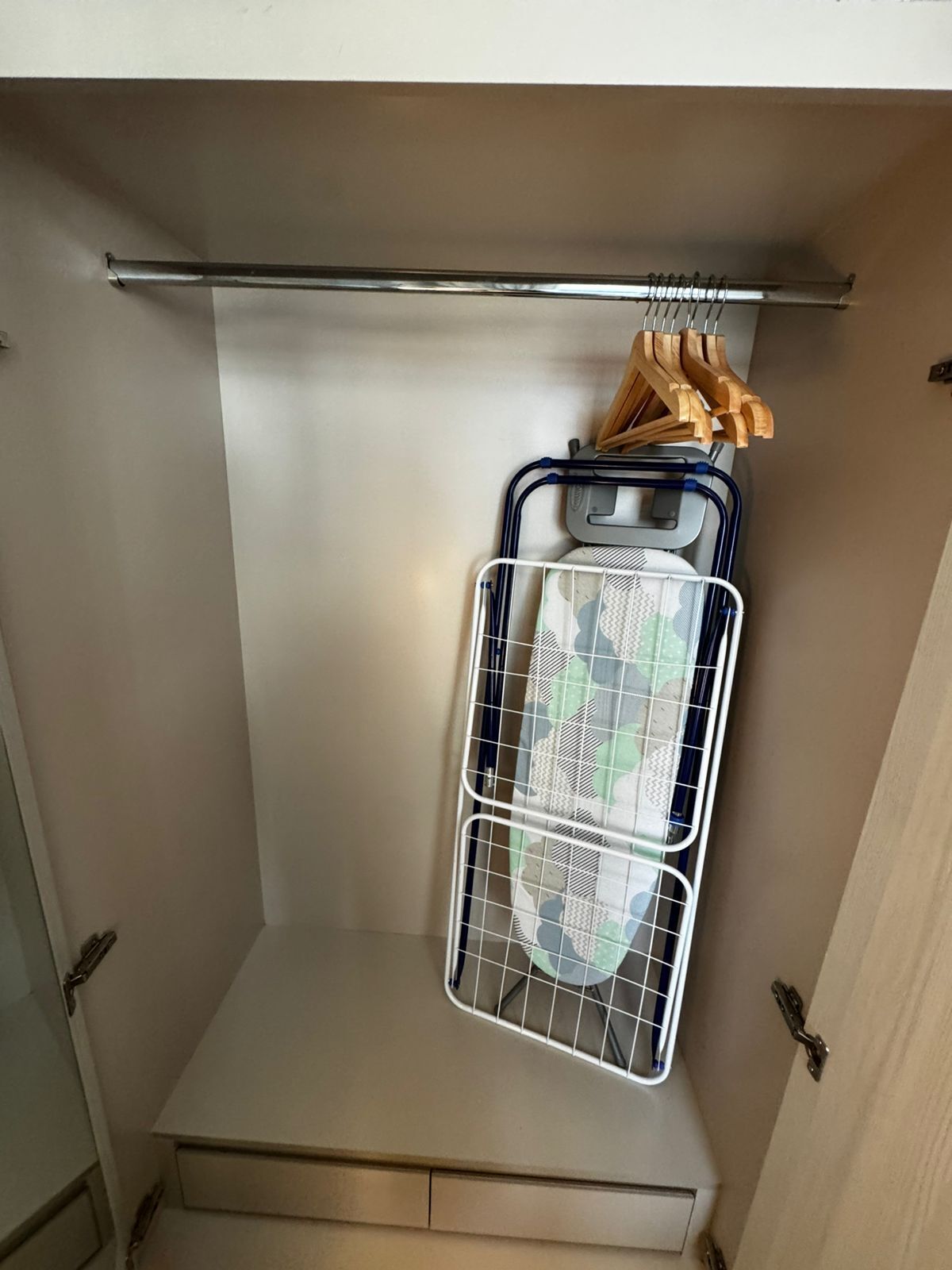 Un espacio de almacenamiento con una estantería metálica que sostiene una cesta y perchas de madera.