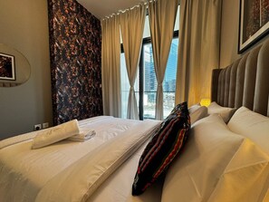 A hotel room with a bed, a window with curtains, a floral wallpaper, and a city view. - Stylish 1BR Lake View Retreat  (Dubai)