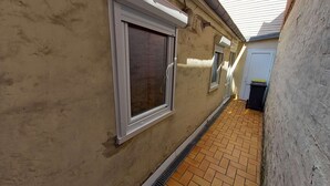Un estrecho pasillo con suelo de baldosas y una ventana con marco blanco.