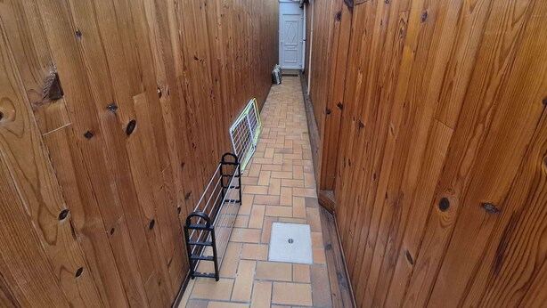 Un estrecho pasillo de madera con un perchero metálico y una puerta al final.