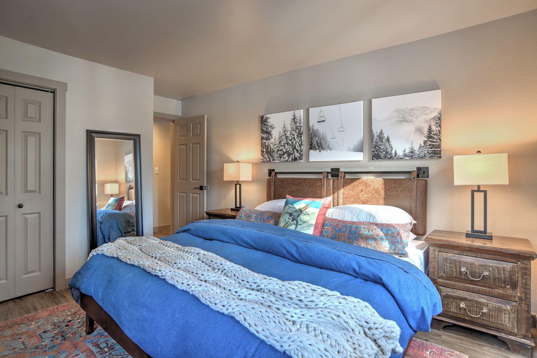 A bedroom with a large bed, two bedside tables, a dresser, and three wall-mounted pictures.